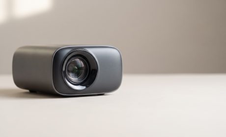 Videoproiettore compatto su fondo neutro, confronto tra proiettore e TV per il salotto